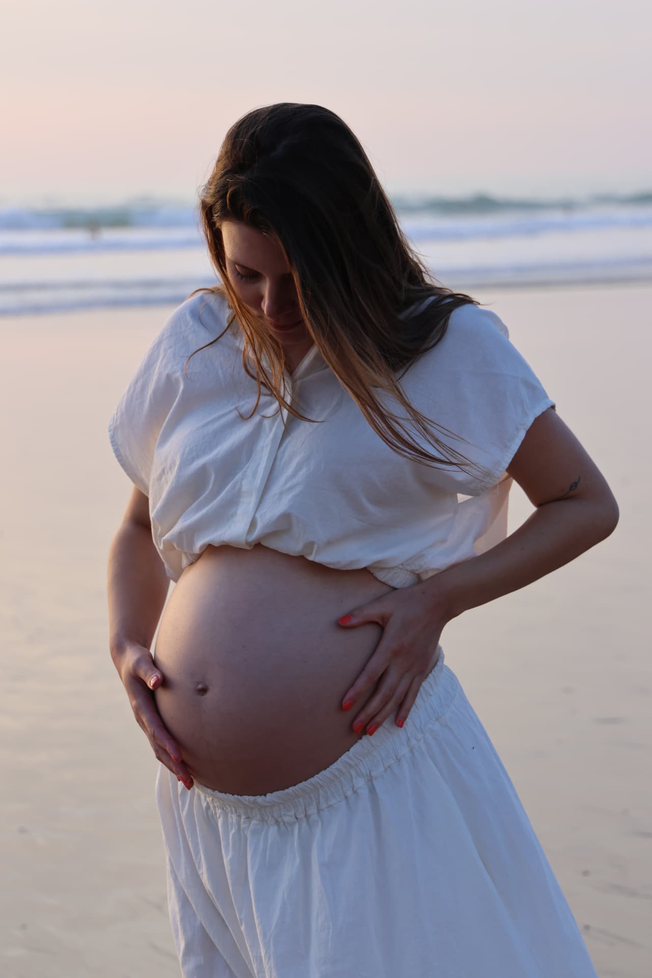 Future maman en tenue blanche tenant son ventre sur la plage au crépuscule
