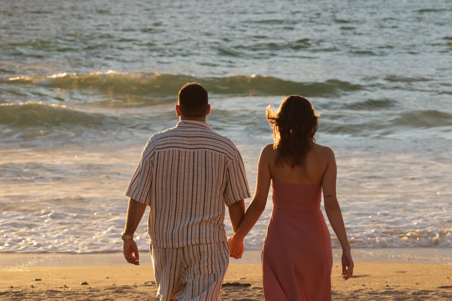 Couple de dos, main dans la main, marchant sur la plage au coucher du soleil près de La Rochelle