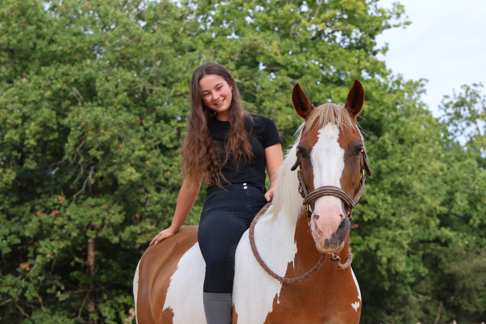 Cavalière en selle souriant face à l'objectif, arbres en arrière-plan
