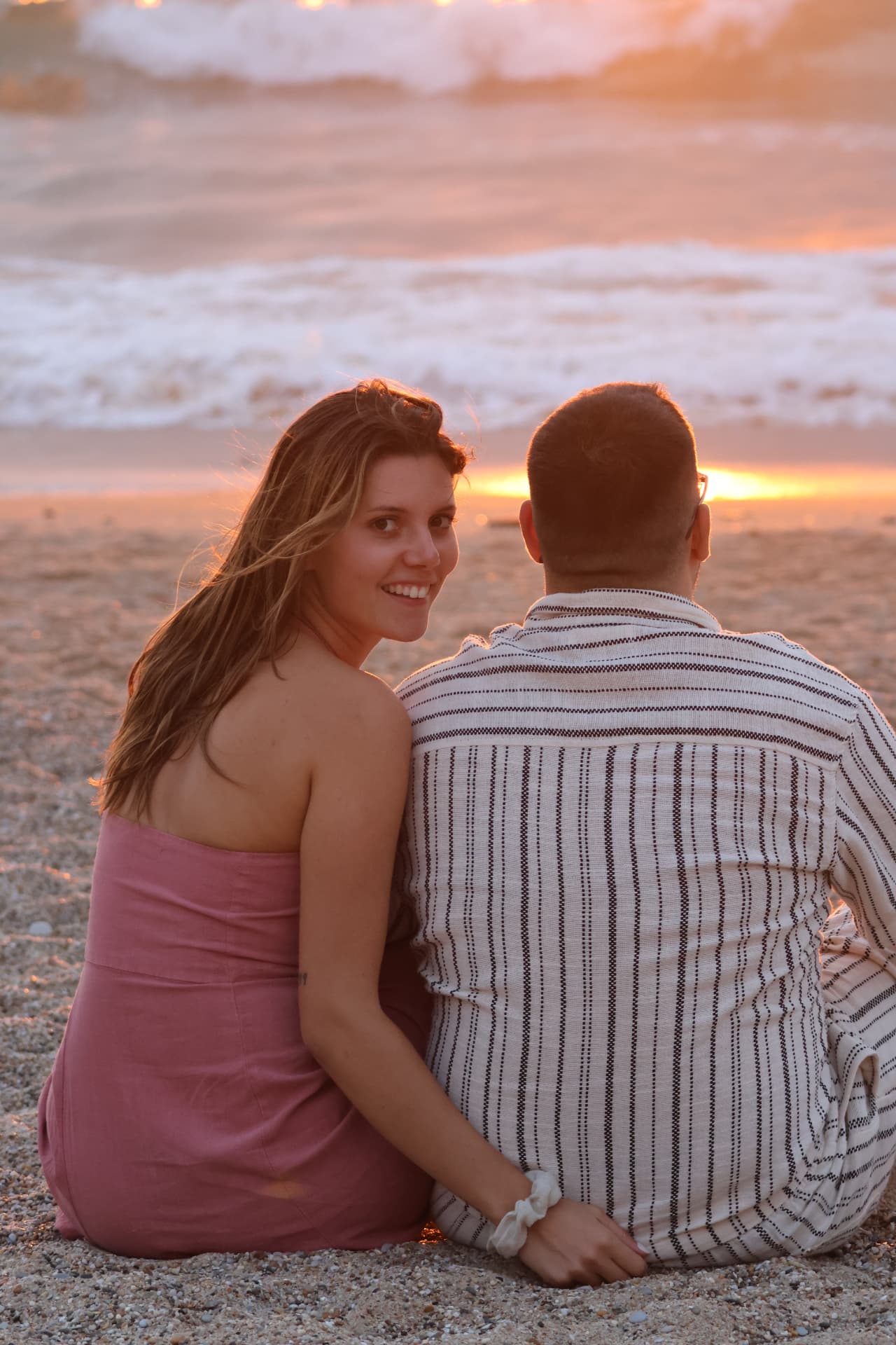 Couple assis dans le sable, la femme se retourne et sourit à l'objectif